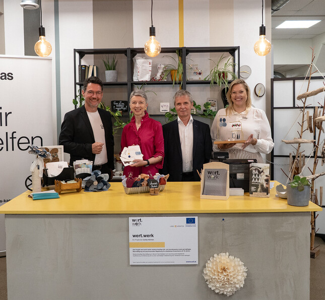 Mehrere Personen stehen hinter einem Tisch mit Produkten aus Arbeitsprojekten bei einer Veranstaltung.