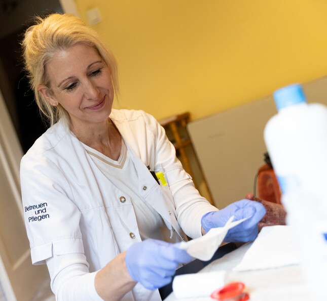 Eine Pflegekraft öffnet mit Handschuhen einen frischen Verband und lächelt dabei.