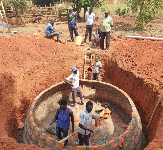 Mehrere Personen errichten eine gemauerte Biogasanlage in einer Baugrube als Teil eines Entwicklungsprojekts.