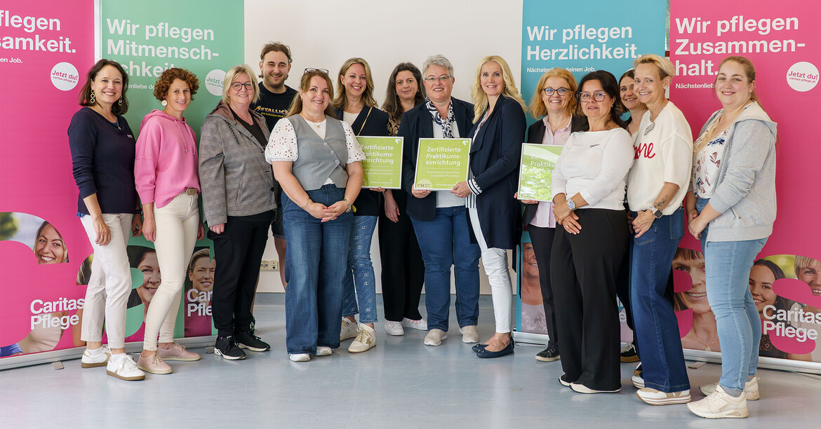 Gruppe von Mitarbeitenden hält Zertifikate vor Caritas Pflege Roll-ups mit den Slogans Wir pflegen Menschlichkeit, Herzlichkeit und Zusammenhalt