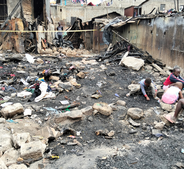 Kinder sitzen zwischen Trümmern und verbrannten Gebäuden nach einem Brand in einer Siedlung.