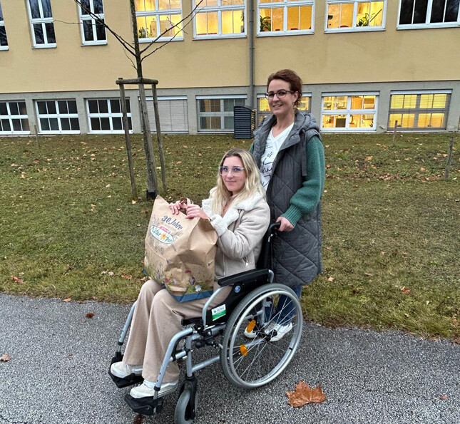 Schülerin begleitet eine Person im Rollstuhl bei einer sozialen Aktion im Außenbereich der Schule.