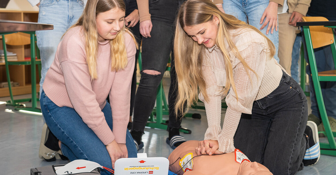 Schüler*innen trainieren Wiederbelebung mit Defibrillator an einer Übungspuppe im Unterricht.