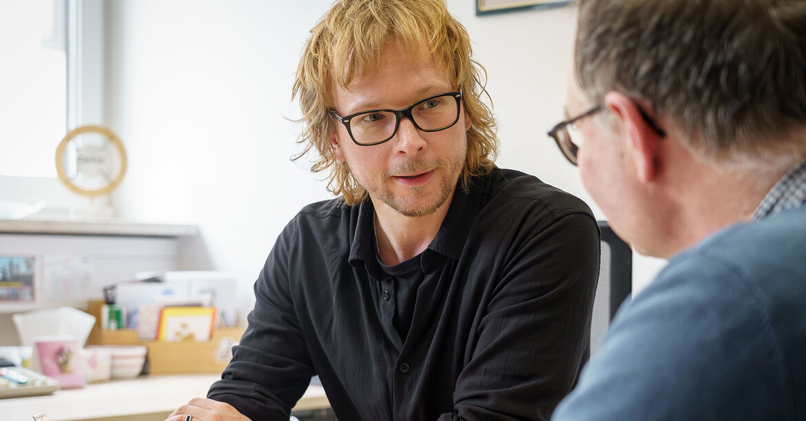 Zwei erwachsene Personen sitzen einander an einem Tisch gegenüber. 