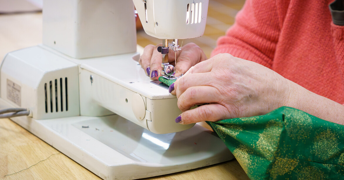 Hände führen Stoff unter einer Nähmaschine bei einer handwerklichen Tätigkeit