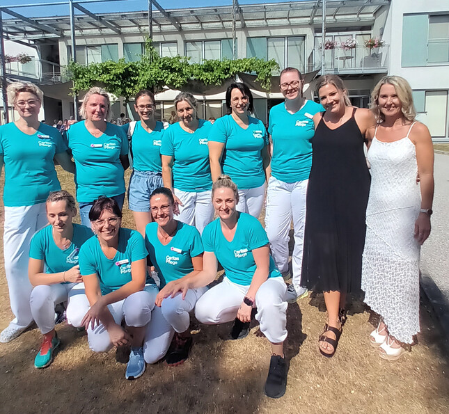 Pflegeteam steht gemeinsam im Freien vor einem Pflegewohnhaus bei einer Jubiläumsfeier