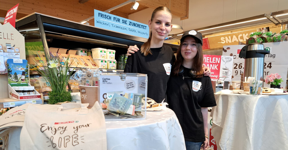Zwei Jugendliche mit SPAR Coffee to help-TShirts stehen neben zwei Stehtischen mit Spendenbox und Kaffeekanne.