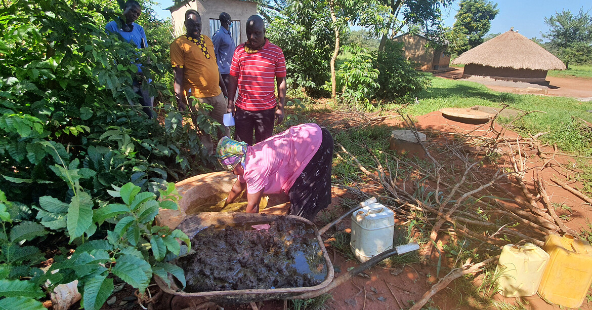 Personen füllen organisches Material in eine Biogasanlage neben Wohnhäusern und Feldern.