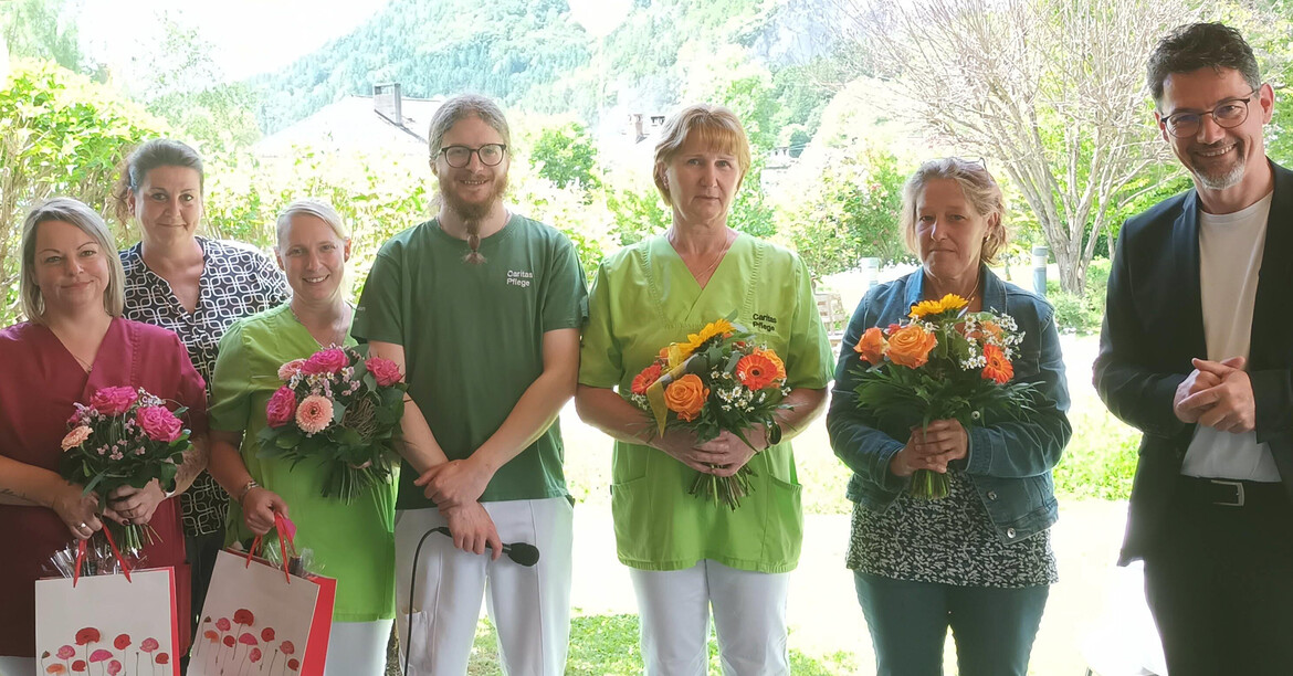 Mitarbeiter*innen des Haus Anna stehen mit Blumen auf der Terrasse, neben ihnen der Caritasdirektor Ernst Sandriesser.