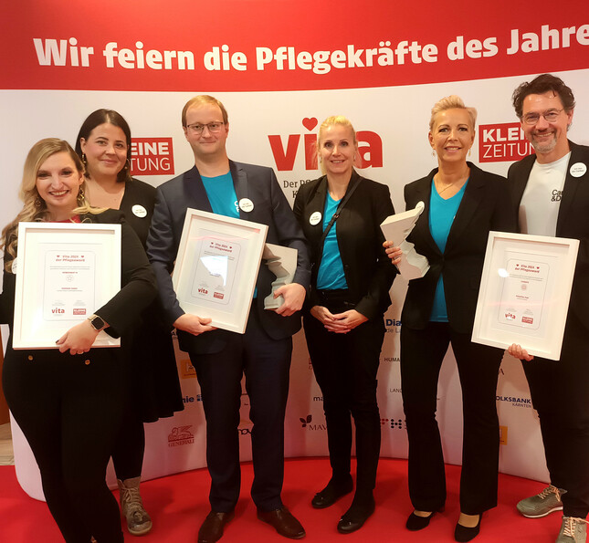 Die Gewinner*innen des VITA Awards stehen mit ihren Leitungen glücklich und mit ihren Preisen in den Händen vor einem großen Transparent.