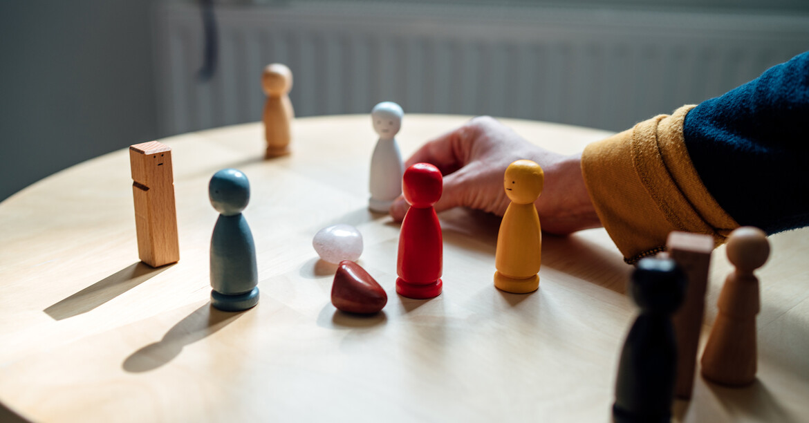Holzfiguren auf einem Tisch symbolisieren familiäre Beziehungen und gemeinsame Lösungsfindung in der Beratung.