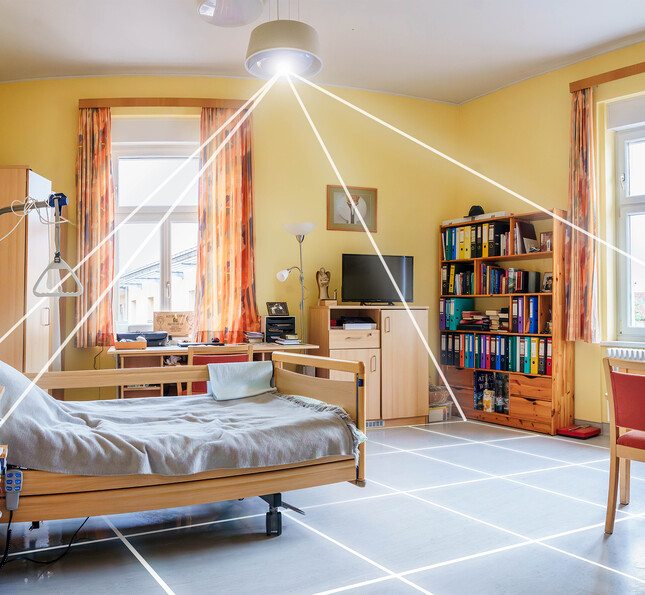 Pflegezimmer mit Pflegebett, Möbeln und Deckenleuchte, die den Raum technisch überwacht und den Alltag unterstützt