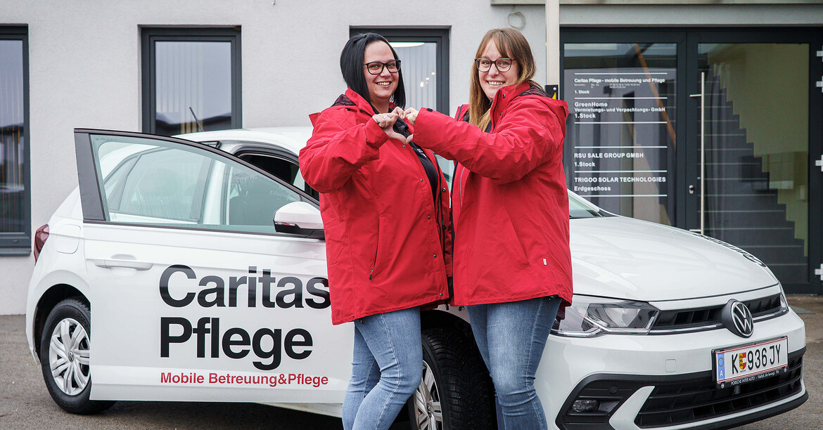 Zwei Pflegekräfte stehen vor einem Auto mit Aufschrift Caritas Pflege – Mobile Betreuung und Pflege.