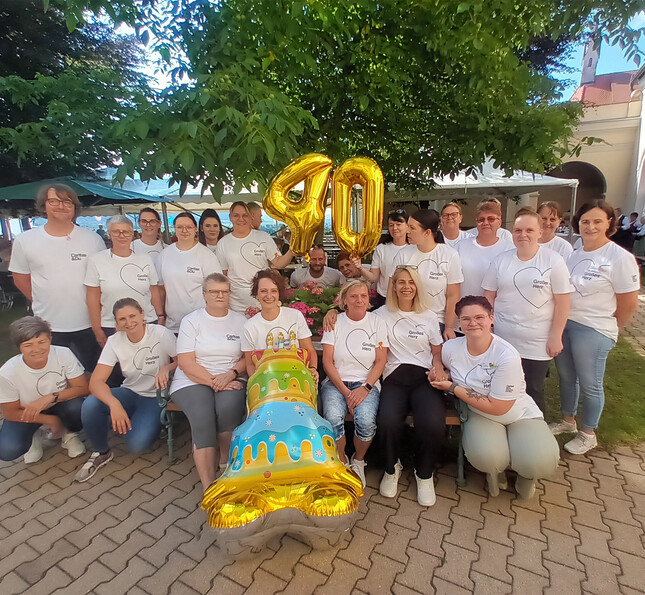 Mitarbeiter*innen des Haus Elisabeth in St. Andrä stellen sich mit Luftballon-Torte und der Zahl 40 im Garten des Hauses auf.
