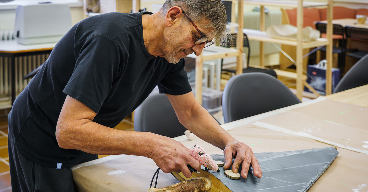 Person bearbeitet Holz und Material an einem Tisch mit Werkzeug in einer Werkstatt