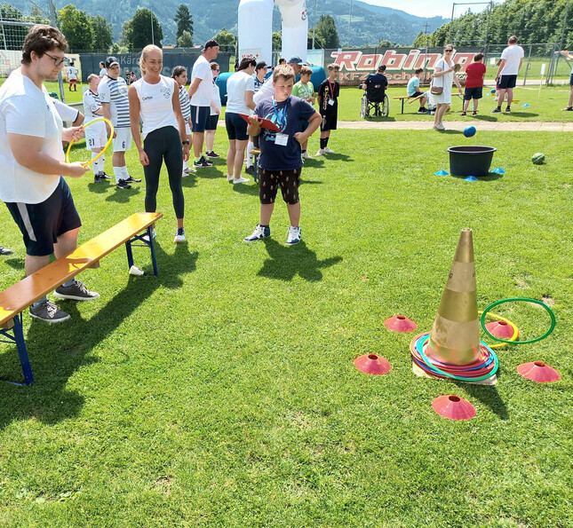 Ein Klient des Caritas-Team Lebensgestaltung wirft Ringe auf ein Hüttchen ein Junge zählt dabei die Punkte. Im Hintergrund sieht man viele andere Sportbegeisterte.