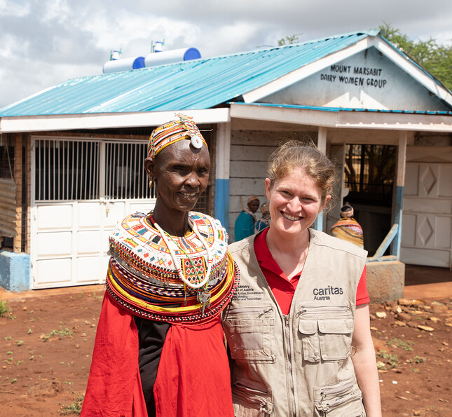 Projektreferentin Theresa Sacher steht mit einer afrikanischen Frau vor einer Hütte auf dem trocken afrikanischem Boden.