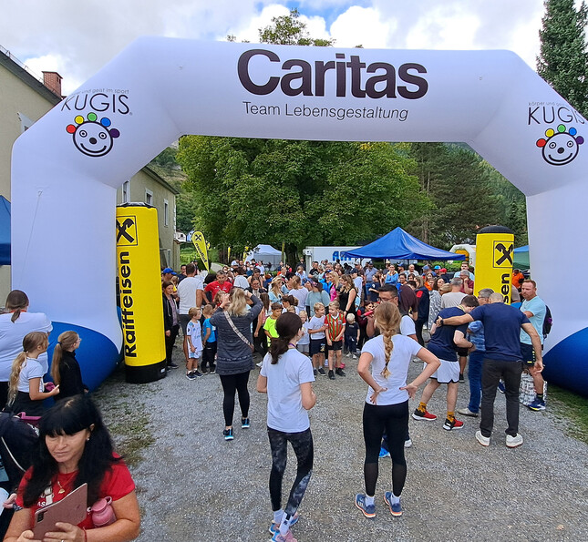 Viele Läuferinnen und Besucherinnen sammeln sich unter dem Caritas-Startbogen beim Charity Run.