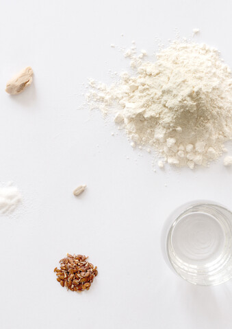 Die verschiedenen Zutaten für Brot liegen auf einem weißen Grund: Mehl, Wasser, Salz, Germ, Samen und Backpulver.