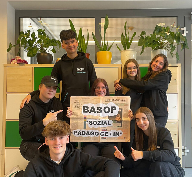 Studierende halten ein Plakat mit der Aufschrift „BASOP Sozialpädagog*in“ in einem Klassenraum.