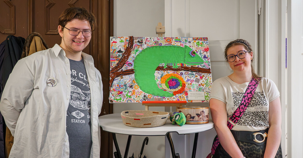 Zwei Personen stehen neben einem ausgestellten Kunstwerk bei einer Vernissage der Caritas.