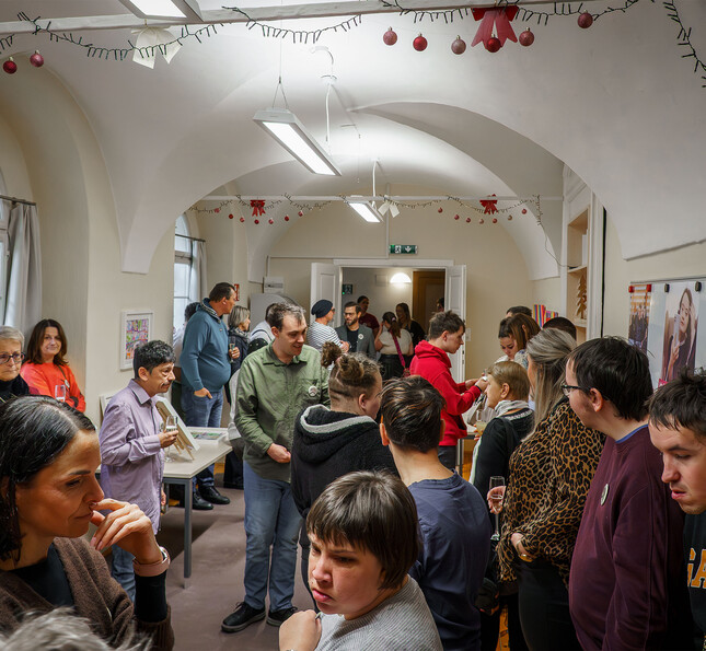 Besucher*innen stehen in einem Raum und tauschen sich bei einer Vernissage der Caritas aus.